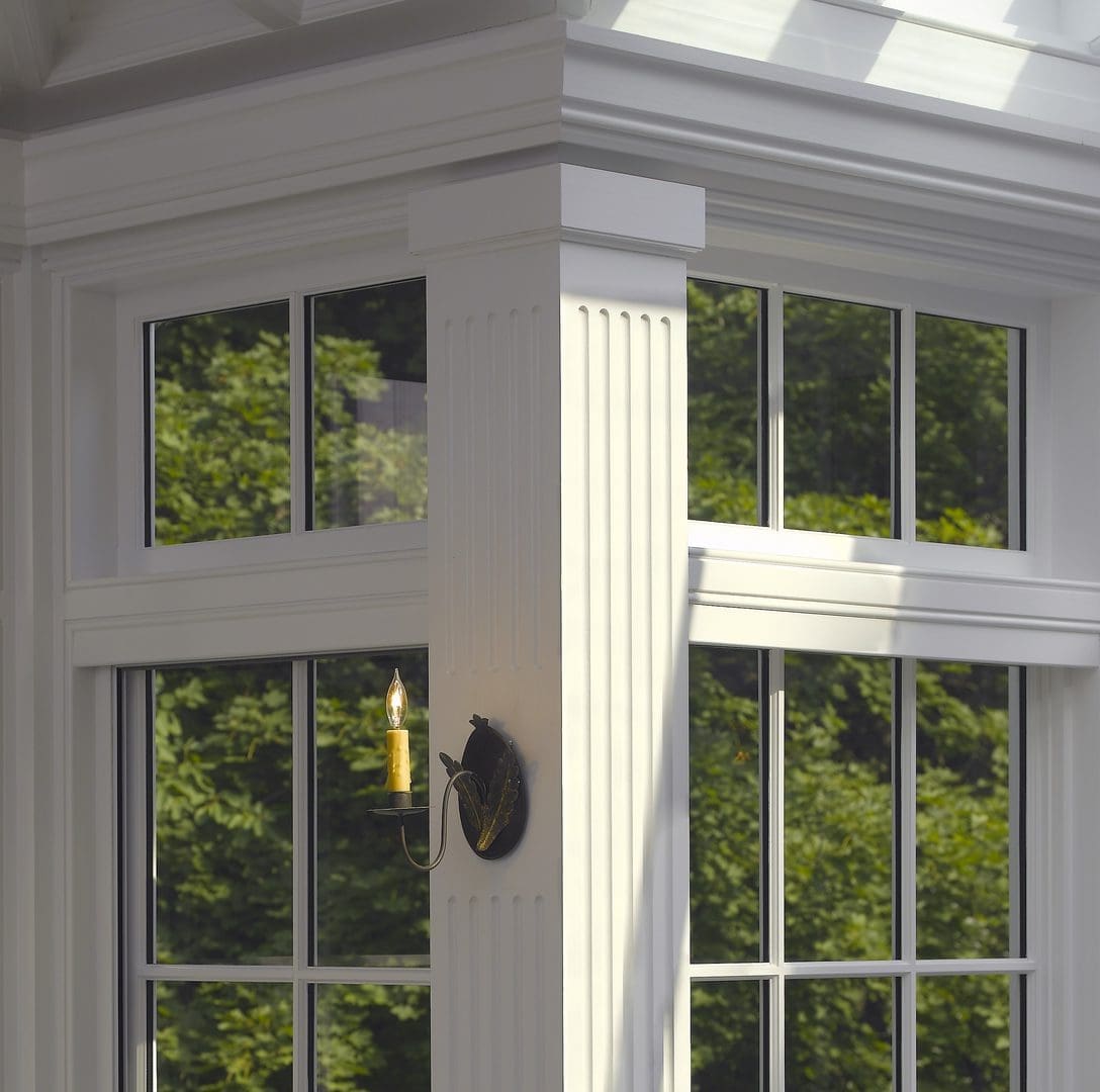 A corner of a room with two windows and trees in the background.