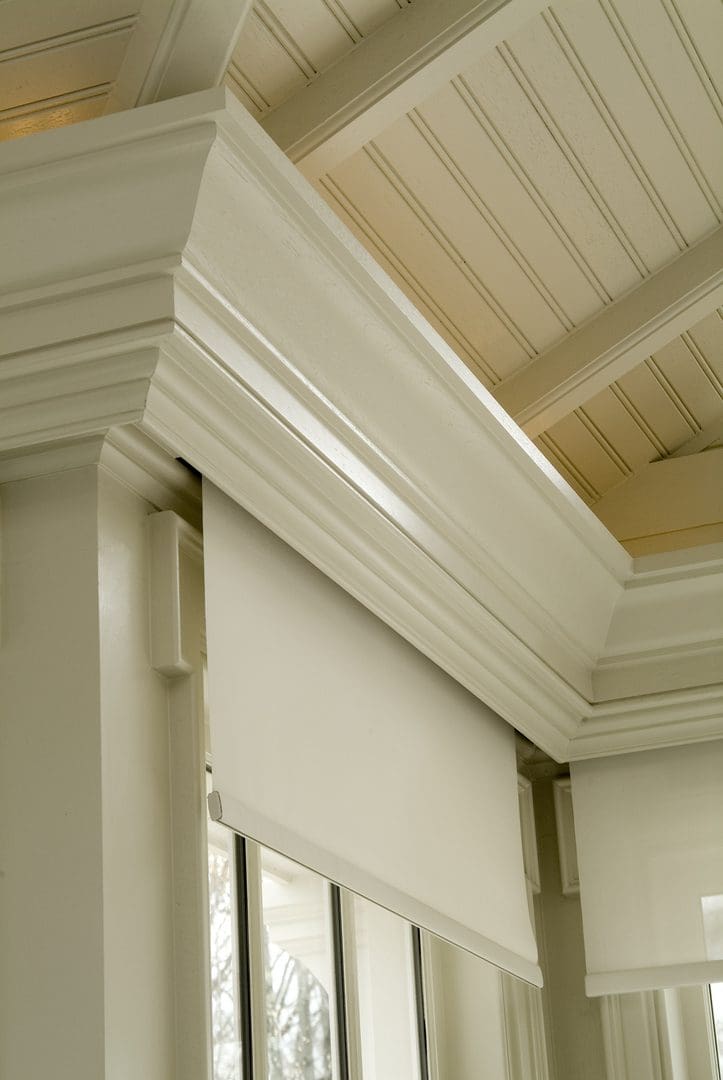 A white roller shade in the corner of a room.