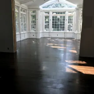 A room with dark wood floors and large windows.